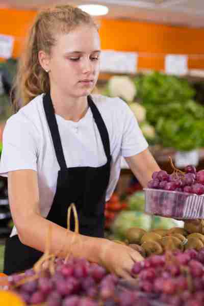 A young girl working at a grocery store stocking produce.